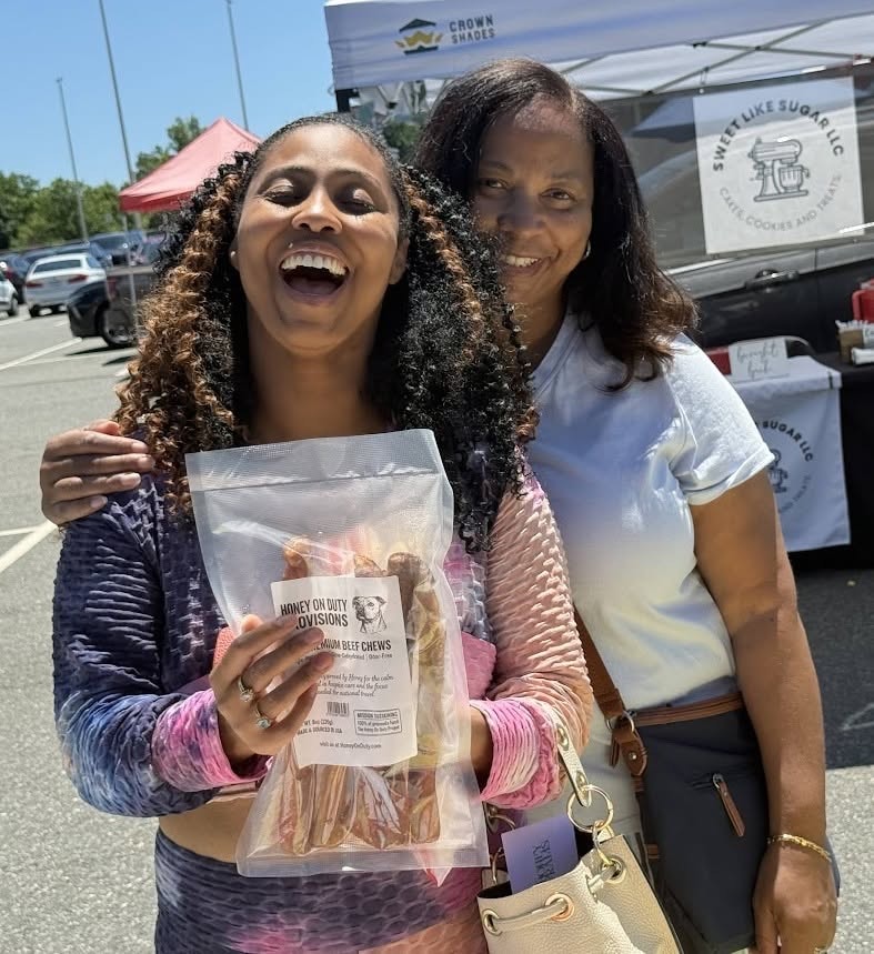 Two women holding Honey's Dog Treats cards at a local market