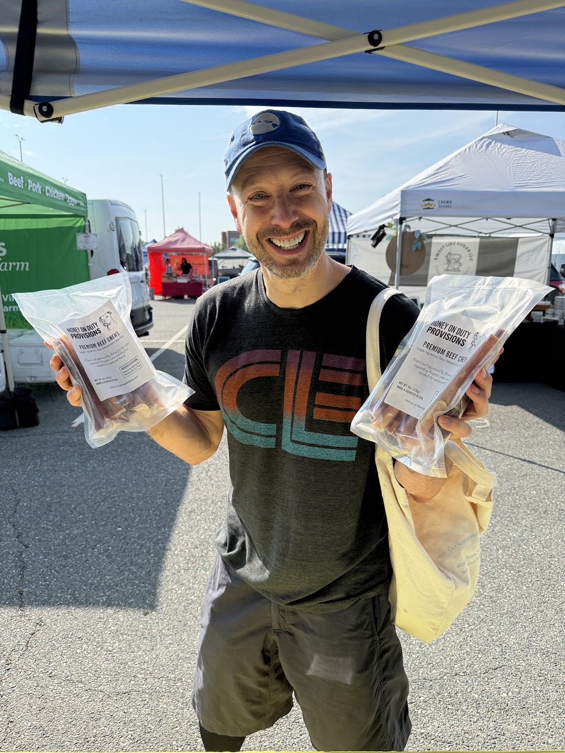 A happy customer holding two packs of Honey's Dog Treats at a local market booth