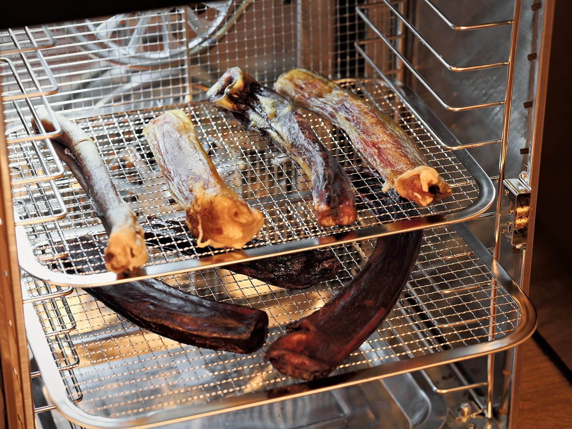 Beef pizzle chews laid out on smoker drying racks in Honey's Small Kitchen